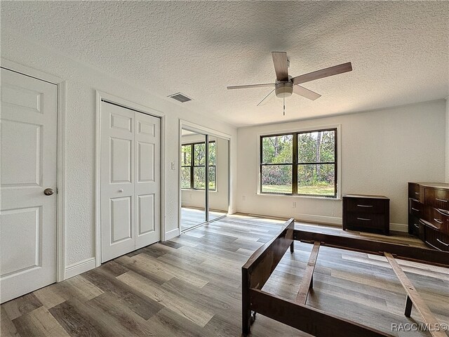 bedroom with visible vents, ceiling fan, wood finished floors, a textured ceiling, and multiple closets