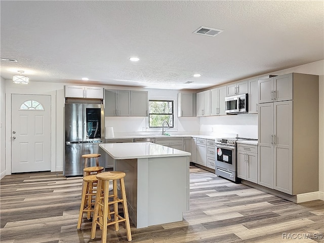 kitchen with appliances with stainless steel finishes, a kitchen island, visible vents, and gray cabinetry