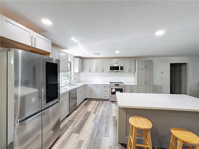 kitchen featuring a breakfast bar area, light countertops, appliances with stainless steel finishes, light wood-style floors, and a sink