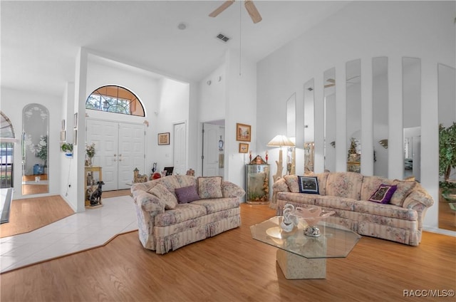 living room featuring a towering ceiling, ceiling fan, visible vents, and wood finished floors