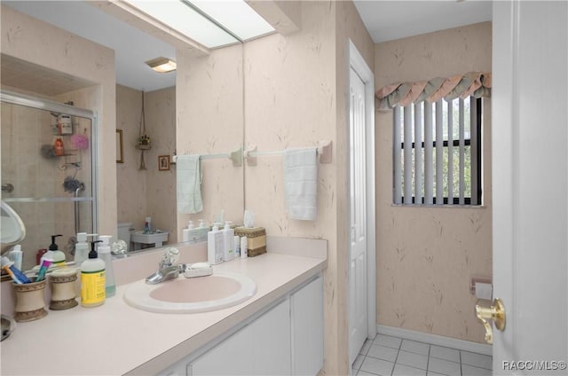 bathroom featuring a skylight, a stall shower, vanity, baseboards, and tile patterned floors