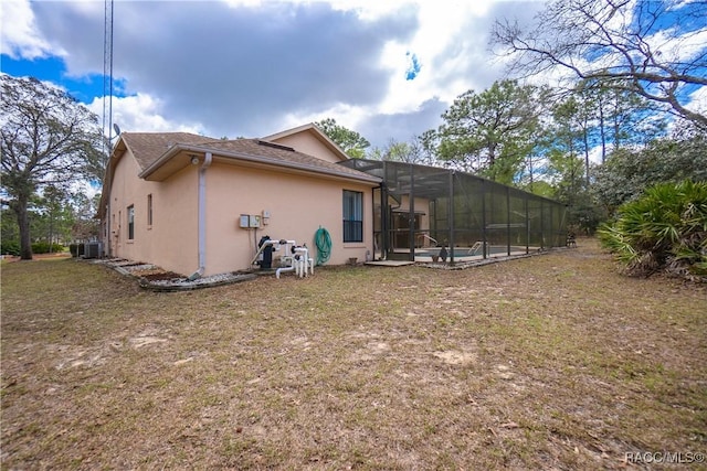 rear view of property featuring glass enclosure, a lawn, and stucco siding