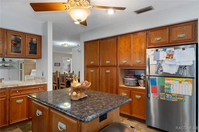 kitchen featuring ceiling fan, a kitchen island, dark stone countertops, and stainless steel refrigerator