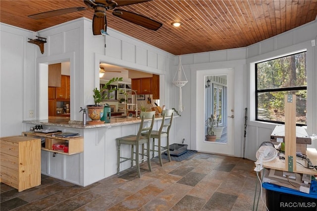 kitchen with light stone countertops, kitchen peninsula, a breakfast bar area, and wooden ceiling