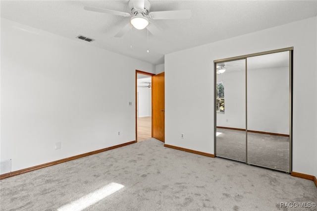 unfurnished bedroom with a textured ceiling, light colored carpet, a closet, and ceiling fan