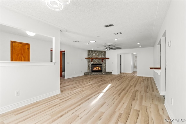 unfurnished living room with a stone fireplace, ceiling fan, light hardwood / wood-style floors, and a textured ceiling