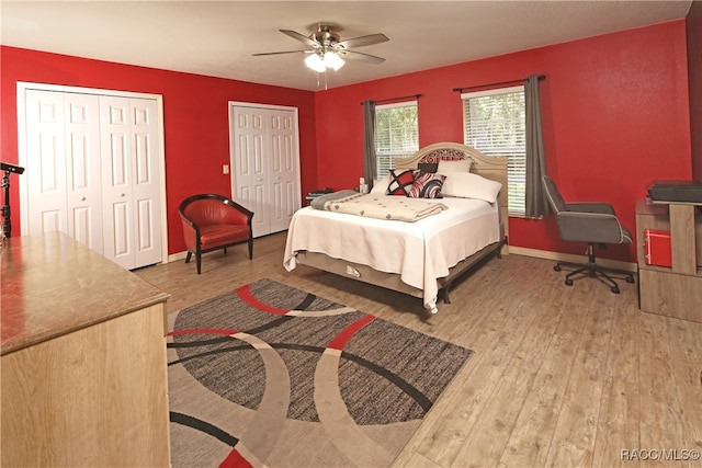 bedroom with hardwood / wood-style flooring, ceiling fan, and multiple closets