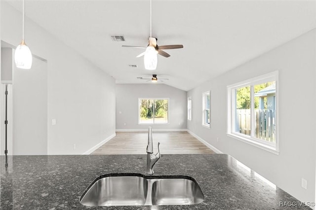 kitchen with pendant lighting, lofted ceiling, dark stone counters, and sink