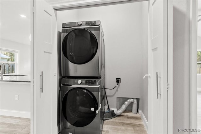 clothes washing area featuring sink, light hardwood / wood-style floors, and stacked washer and clothes dryer