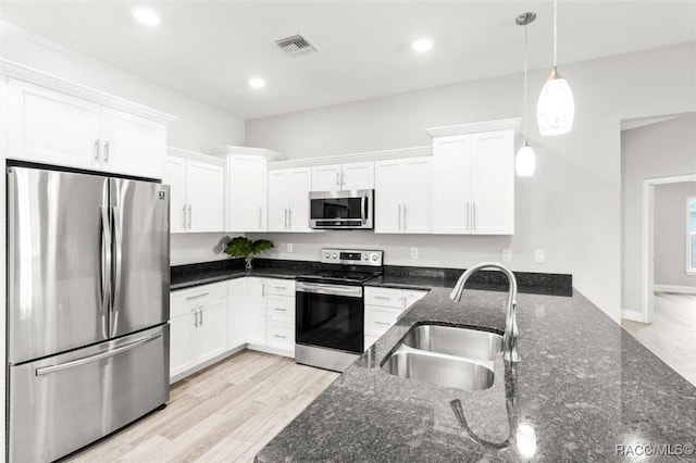 kitchen featuring decorative light fixtures, sink, white cabinets, stainless steel appliances, and light wood-type flooring