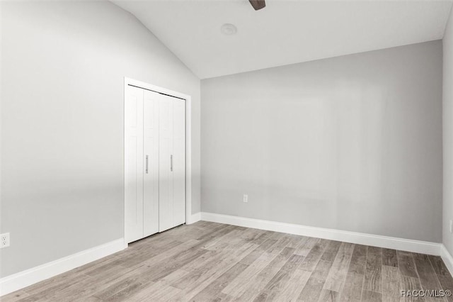 unfurnished bedroom featuring ceiling fan, vaulted ceiling, a closet, and light wood-type flooring