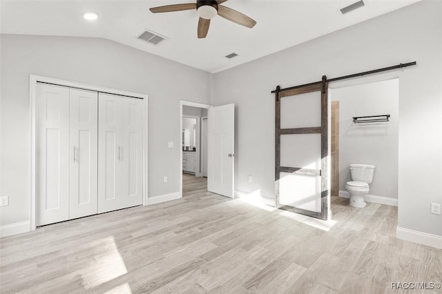 unfurnished bedroom with ensuite bath, light wood-type flooring, a closet, ceiling fan, and a barn door