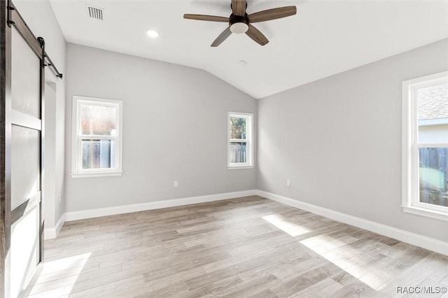 spare room featuring ceiling fan, a barn door, vaulted ceiling, and light wood-type flooring