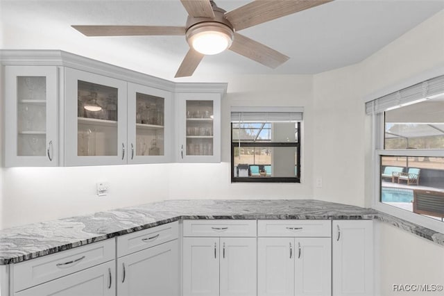 kitchen with light stone counters, ceiling fan, and white cabinets