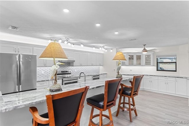 kitchen featuring a breakfast bar area, appliances with stainless steel finishes, light stone countertops, white cabinets, and decorative backsplash