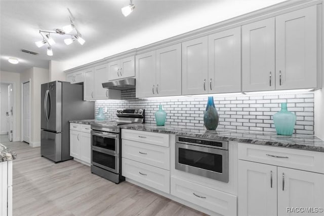 kitchen with tasteful backsplash, white cabinets, dark stone counters, stainless steel appliances, and light wood-type flooring