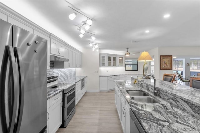 kitchen with appliances with stainless steel finishes, white cabinetry, sink, decorative backsplash, and light stone counters