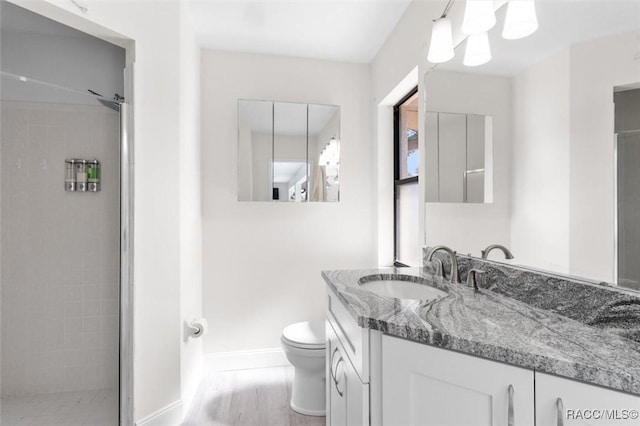 bathroom with hardwood / wood-style flooring, vanity, toilet, and a tile shower