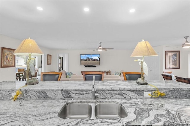 kitchen with light stone counters, ceiling fan, and sink