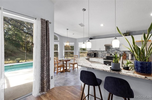 kitchen featuring appliances with stainless steel finishes, white cabinetry, hanging light fixtures, light stone counters, and tasteful backsplash