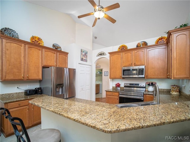 kitchen with light stone countertops, appliances with stainless steel finishes, a kitchen breakfast bar, kitchen peninsula, and vaulted ceiling