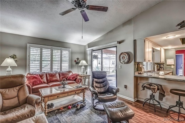 living room with ceiling fan, wood-type flooring, a textured ceiling, and vaulted ceiling