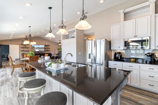 kitchen with hanging light fixtures, stainless steel appliances, a large island with sink, lofted ceiling, and white cabinets