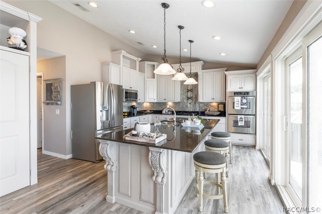 kitchen featuring white cabinets, appliances with stainless steel finishes, light wood-type flooring, and an island with sink