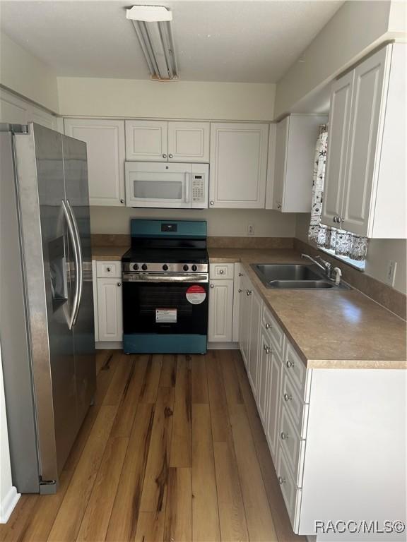 kitchen featuring a sink, stainless steel appliances, wood finished floors, and white cabinetry