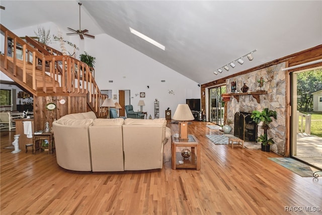 living area with high vaulted ceiling, stairway, wood finished floors, and a stone fireplace