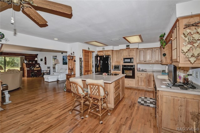 kitchen with a breakfast bar, light countertops, a kitchen island, light wood-type flooring, and black appliances