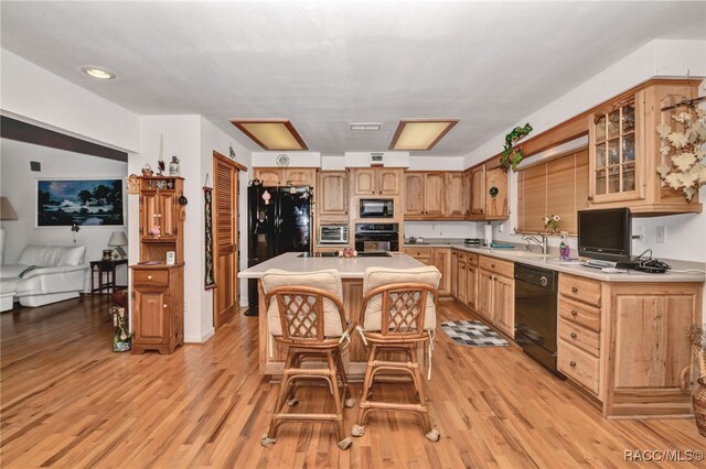 kitchen featuring a sink, black appliances, light wood finished floors, and light countertops