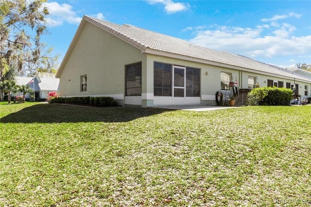 rear view of property featuring a tiled roof, a yard, and stucco siding