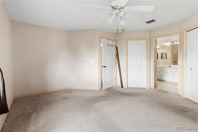 unfurnished bedroom with visible vents, baseboards, ceiling fan, light colored carpet, and ensuite bath