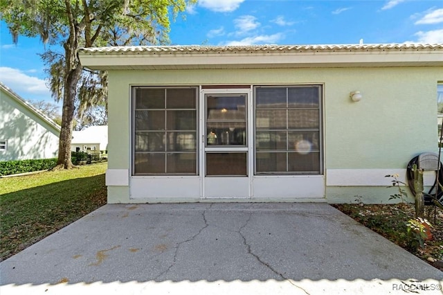 view of exterior entry with stucco siding and a lawn