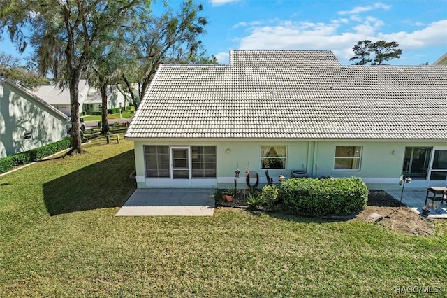 rear view of house with a patio area, a tile roof, a lawn, and stucco siding