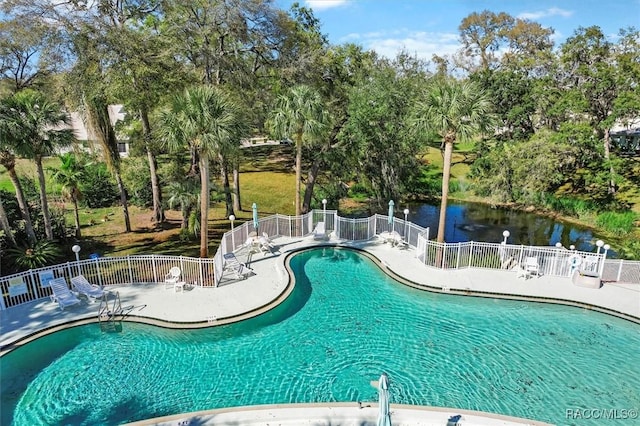 community pool with a patio area, a water view, and fence