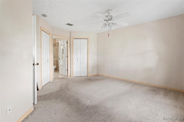 unfurnished bedroom with carpet, visible vents, baseboards, ensuite bathroom, and a textured ceiling