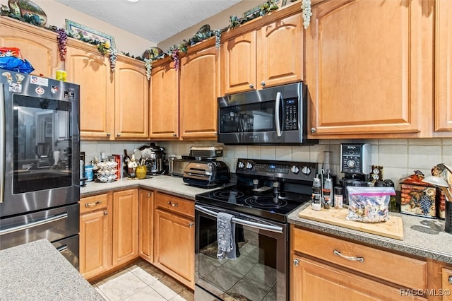 kitchen with appliances with stainless steel finishes, a textured ceiling, tasteful backsplash, and light tile patterned floors