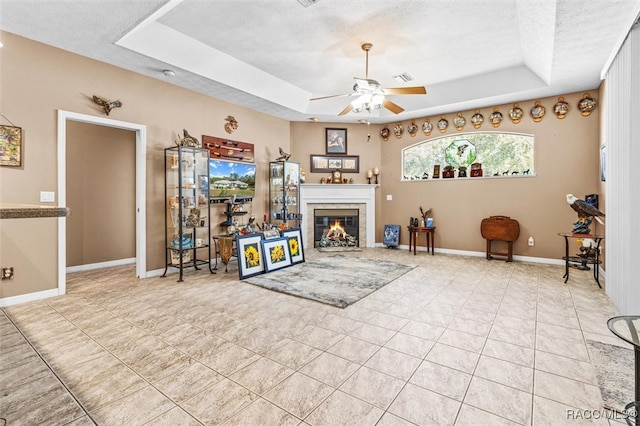 living room featuring a textured ceiling, a tray ceiling, ceiling fan, light tile patterned floors, and a fireplace