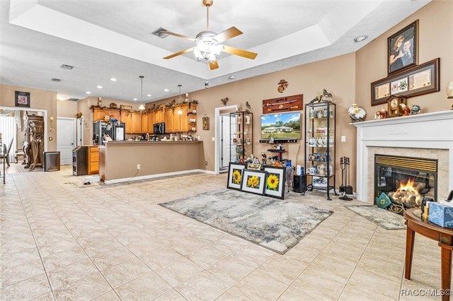 living room featuring a fireplace, a raised ceiling, ceiling fan, and plenty of natural light