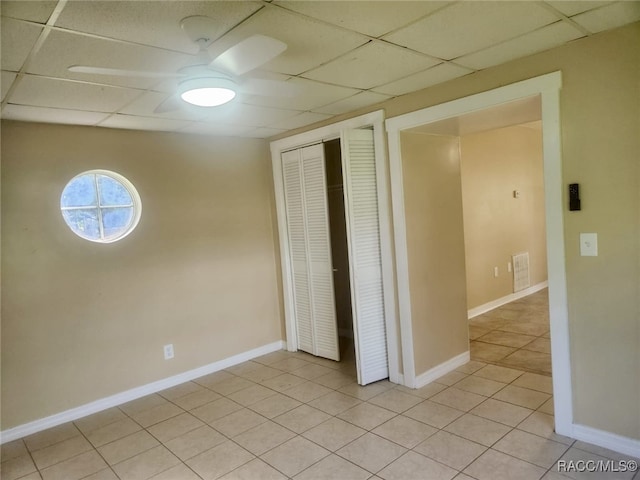 unfurnished bedroom with ceiling fan, a drop ceiling, light tile patterned floors, and a closet