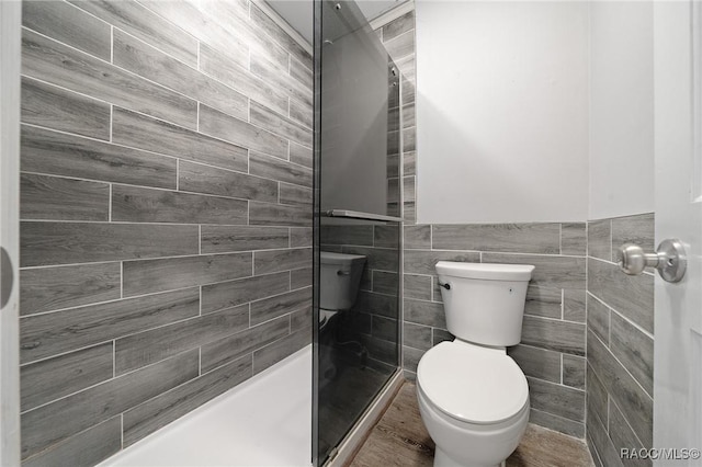 full bath featuring wainscoting, a shower stall, toilet, and tile walls