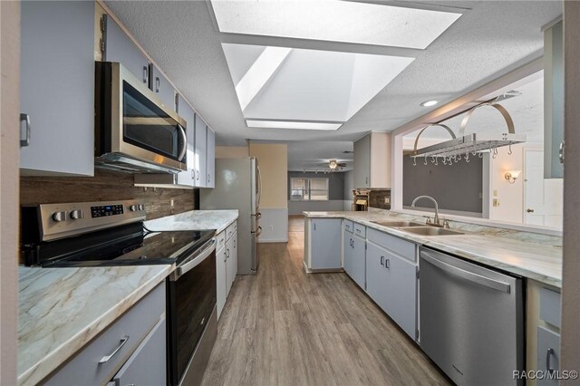 kitchen featuring stainless steel appliances, tasteful backsplash, a skylight, and a sink