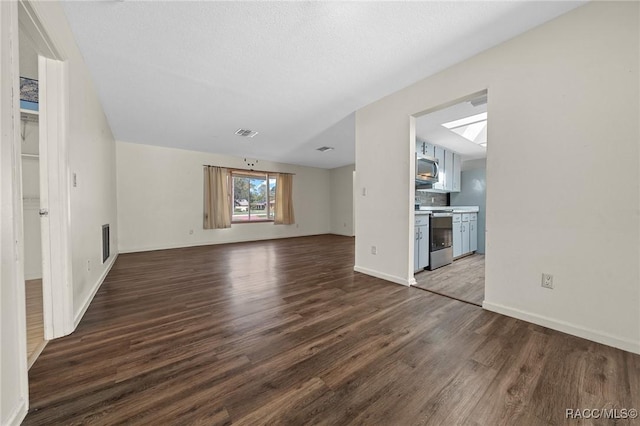 unfurnished living room featuring dark wood-style flooring, visible vents, and baseboards