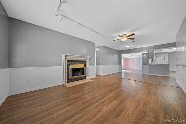 unfurnished living room with visible vents, a tile fireplace, a wainscoted wall, ceiling fan, and wood finished floors