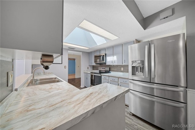 kitchen with a skylight, tasteful backsplash, light countertops, appliances with stainless steel finishes, and a sink