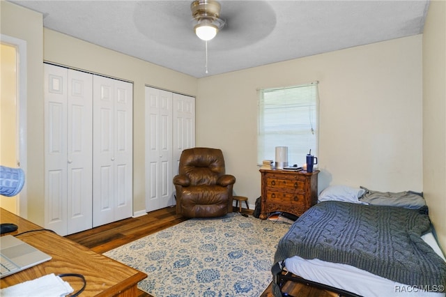 bedroom with ceiling fan, dark hardwood / wood-style flooring, and two closets