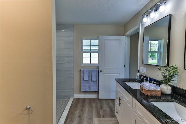 full bathroom with double vanity, a textured ceiling, wood finished floors, and a sink