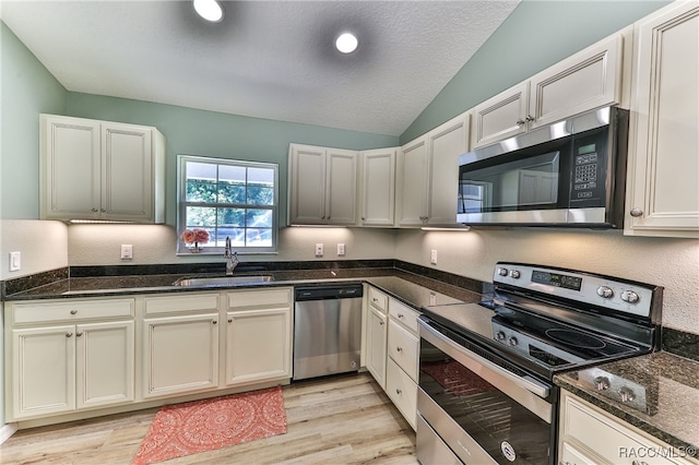 kitchen with dark stone counters, sink, light hardwood / wood-style flooring, vaulted ceiling, and stainless steel appliances